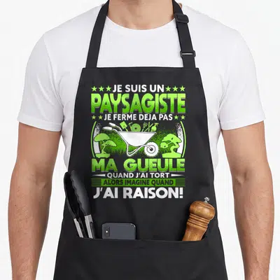 Tablier de cuisine noir avec illustration verte d'une brouette remplie d'outils et texte humoristique sur fond uni.
