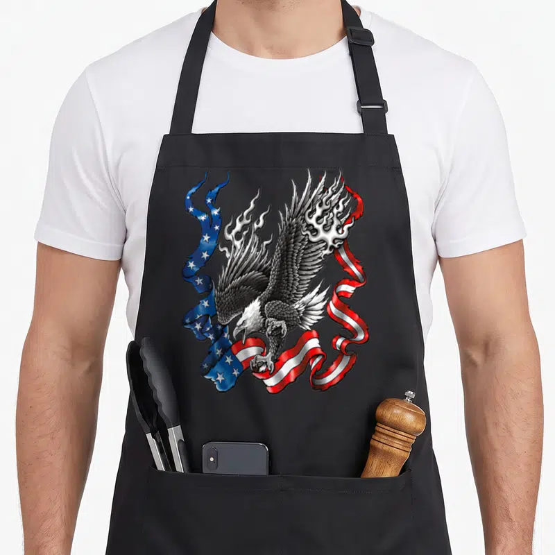 Tablier de cuisine noir avec aigle aux ailes déployées tenant un drapeau américain enflammé dans un style illustration tattoo.