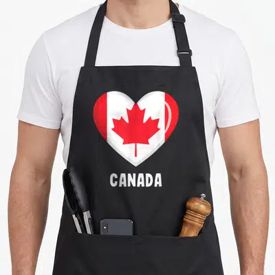 Tablier de cuisine noir avec un grand cœur affichant le drapeau du Canada et le mot CANADA en dessous.