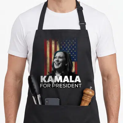 Tablier de cuisine noir avec portrait de Kamala Harris, drapeau USA et texte KAMALA FOR PRESIDENT en blanc.