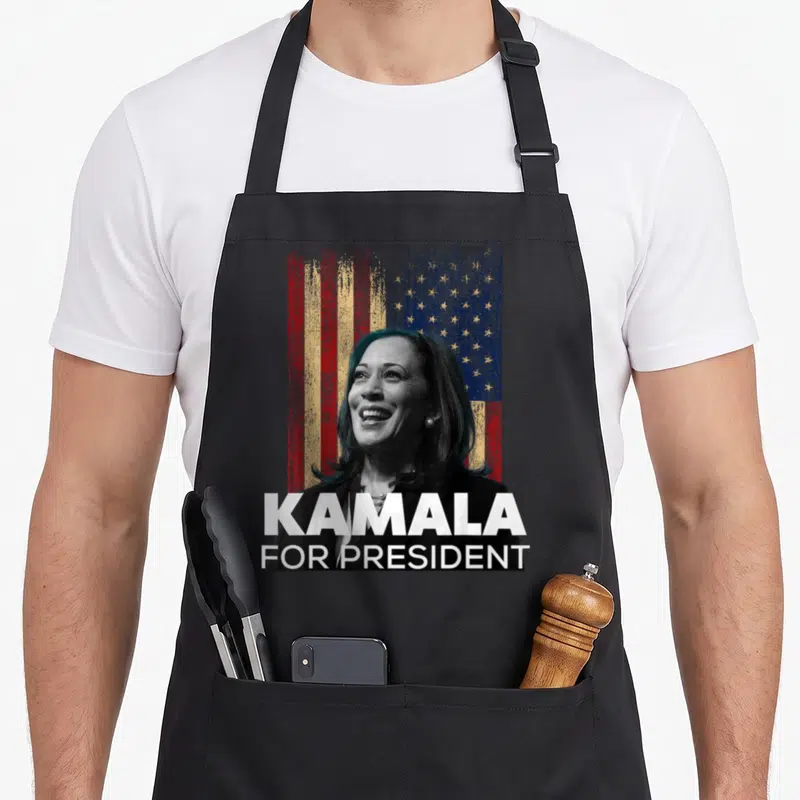 Tablier de cuisine noir avec portrait de Kamala Harris, drapeau USA et texte KAMALA FOR PRESIDENT en blanc.
