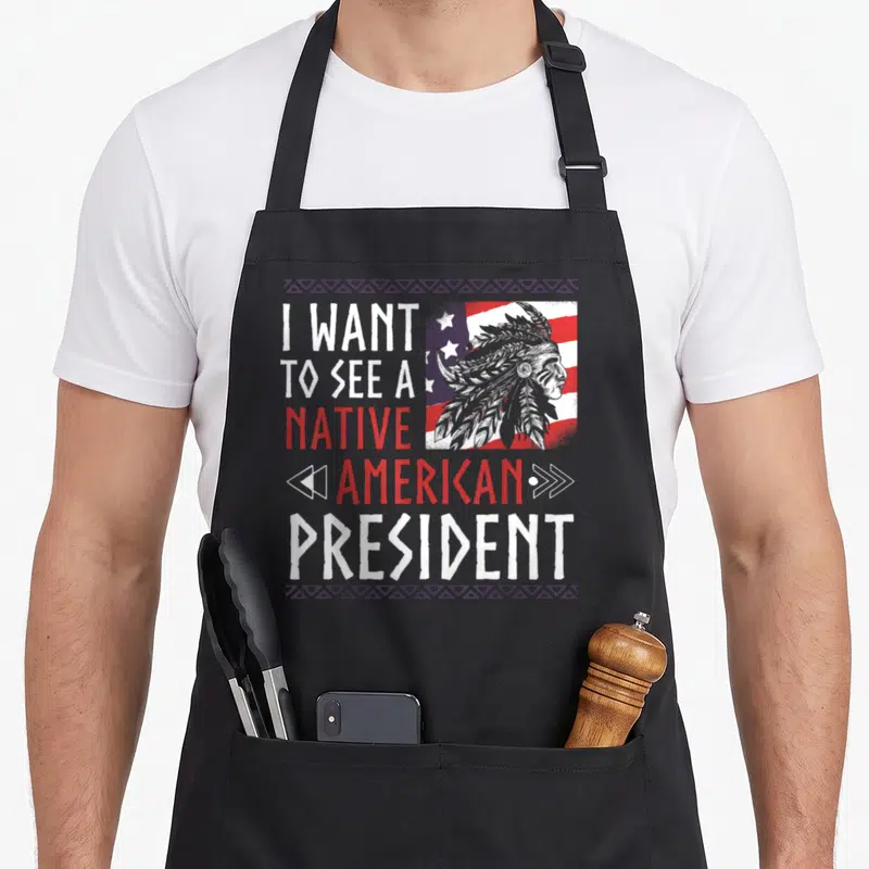 Tablier de cuisine noir avec illustration chef indien et texte I want to see a native american president sur fond de drapeau.