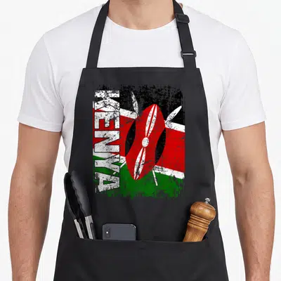 Tablier de cuisine noir avec inscription KENYA verticale, bouclier traditionnel rouge et lances blanches croisées sur fond aux couleurs du drapeau.