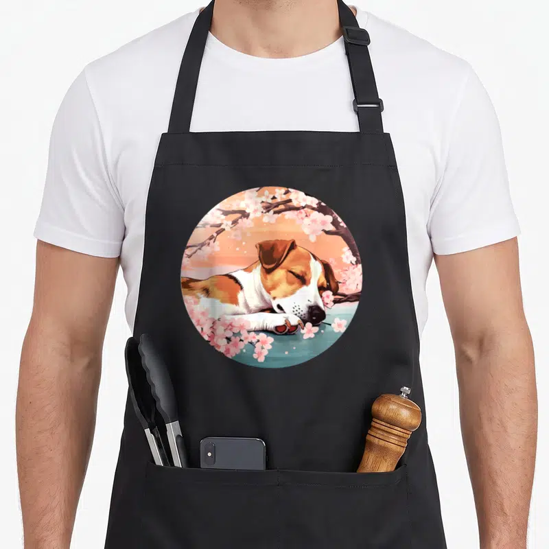 Tablier de cuisine noir avec illustration circulaire d'un chien Jack Russell dormant sous des fleurs de cerisier roses.
