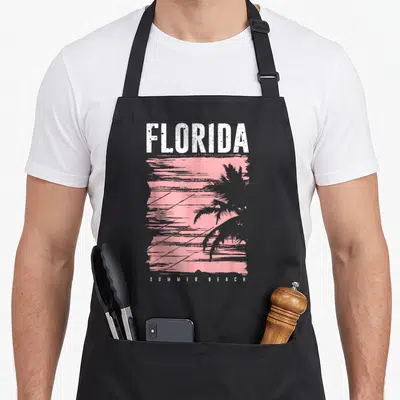 Tablier de cuisine noir avec illustration FLORIDA SUMMER BEACH et silhouette de palmier rose vif.