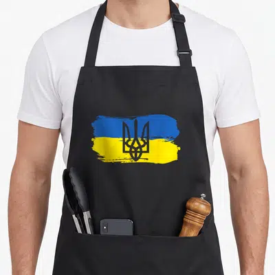 Tablier de cuisine noir avec drapeau ukrainien peint en bleu et jaune et trident gris au centre.