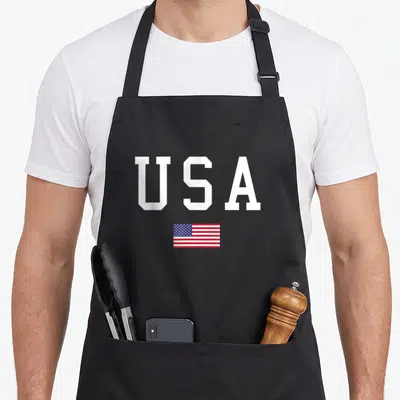Tablier de cuisine noir avec les lettres USA en blanc et un petit drapeau américain vintage imprimé au centre.