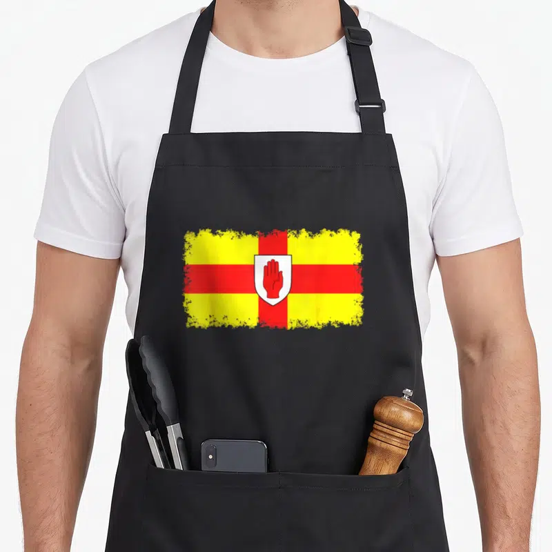 Tablier de cuisine noir avec le drapeau de l'Ulster en jaune et rouge centré par un écu blanc à la main rouge.