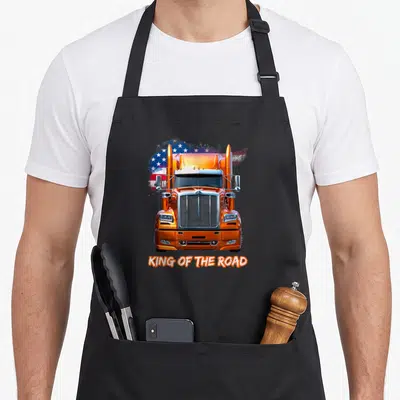 Tablier de cuisine noir avec illustration frontale d'un camion orange et texte King of the Road sur fond de drapeau américain stylisé.