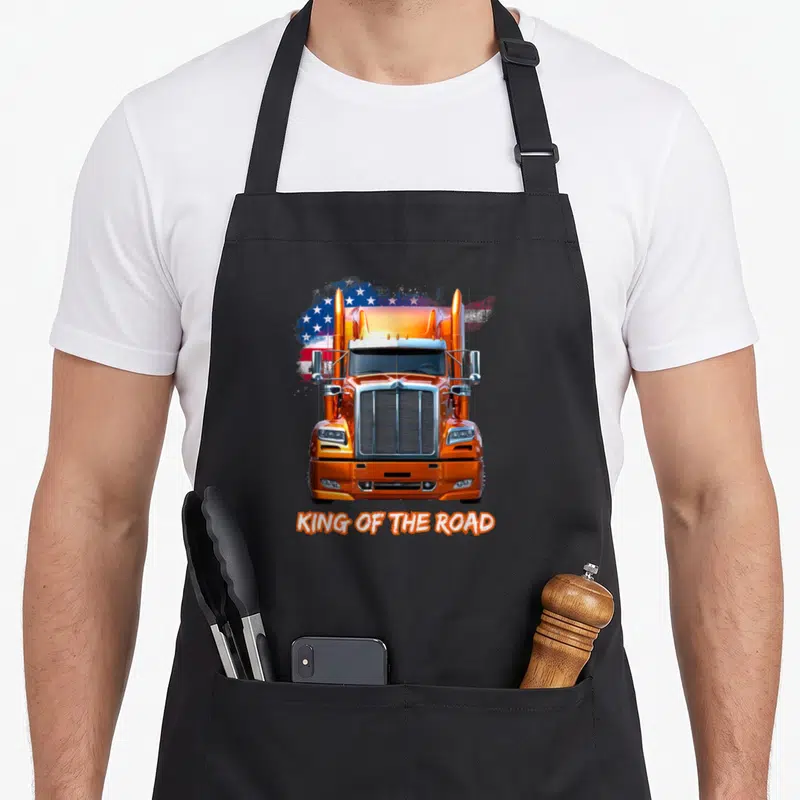 Tablier de cuisine noir avec illustration frontale d'un camion orange et texte King of the Road sur fond de drapeau américain stylisé.