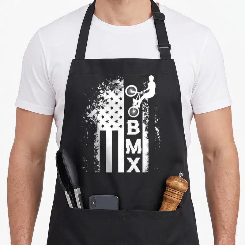 Tablier de cuisine noir avec un drapeau américain stylisé en blanc, une silhouette de cycliste BMX et le texte vertical BMX en style grunge.