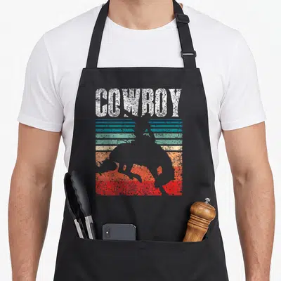 Tablier de cuisine noir avec silhouette cavalier et texte cowboy sur fond de bandes colorées vintage.