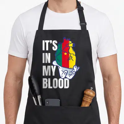 Tablier de cuisine noir avec un cœur aux couleurs du drapeau camerounais et le texte It's In My Blood.