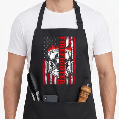 Tablier de cuisine noir avec drapeau américain vintage et casque de pompier croisé avec haches.