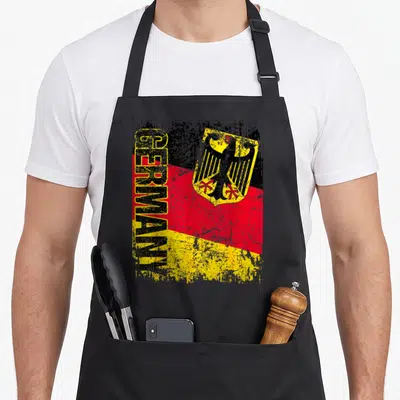 Tablier de cuisine noir avec inscription GERMANY, drapeau tricolore et aigle héraldique jaune sur fond texturé.