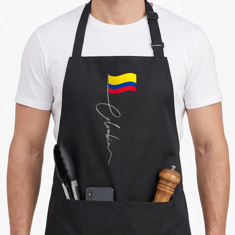 Tablier de cuisine noir avec drapeau colombien ondulant et inscription Colombia en lettres blanches cursives stylisées.