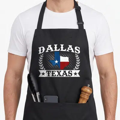 Tablier de cuisine noir avec l'inscription Dallas Texas et une carte du drapeau bleu blanc rouge entourée de branches blanches.