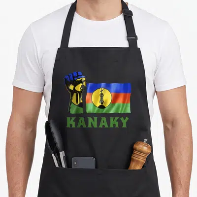 Tablier de cuisine noir avec poing coloré, drapeau Kanaky et texte vert Kanaky en bas.