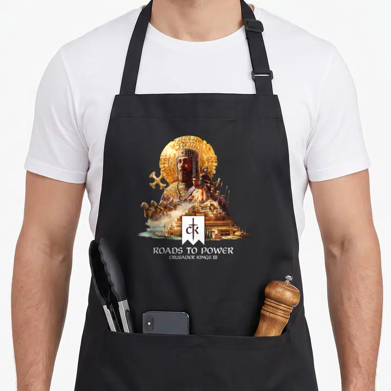 Tablier de cuisine noir avec illustration d'un empereur barbu en armure dorée, cavaliers et château fort au-dessus du texte Roads to Power.