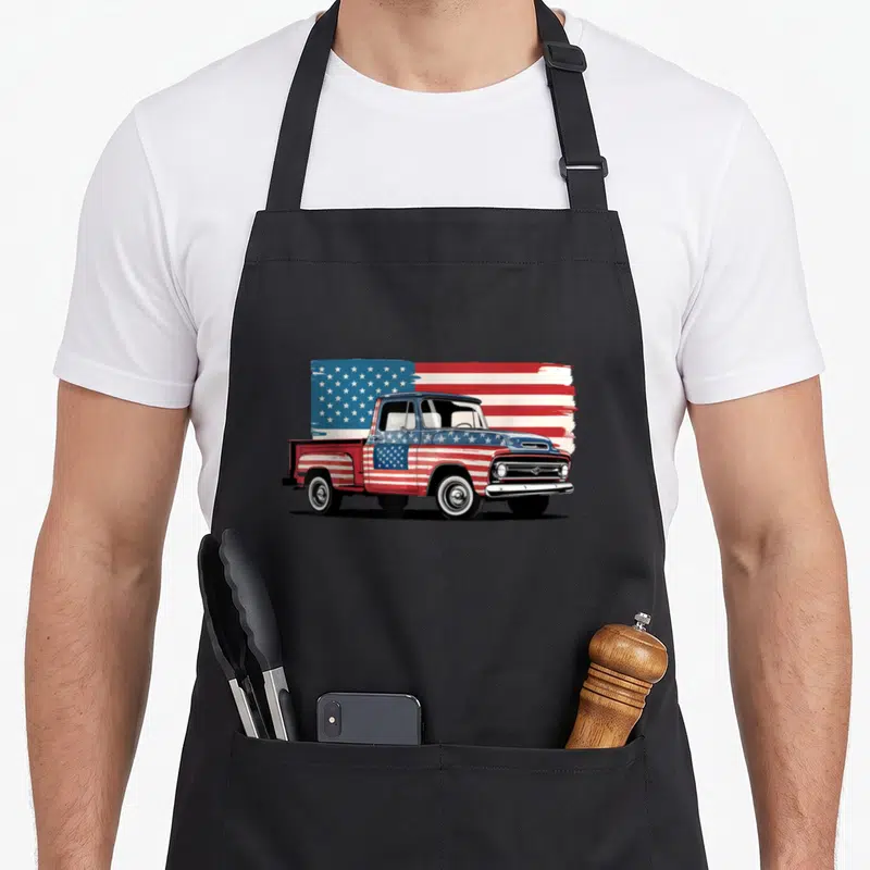 Tablier de cuisine noir avec une illustration de camionnette américaine aux couleurs du drapeau et des étoiles blanches sur fond bleu.