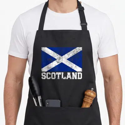 Tablier de cuisine noir avec le drapeau bleu et blanc Scotland et linscription SCOTLAND en lettres blanches usées.