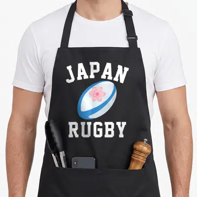 Tablier de cuisine noir avec une balle de rugby japonaise blanche et bleue ornée d'une fleur de sakura rose au centre.