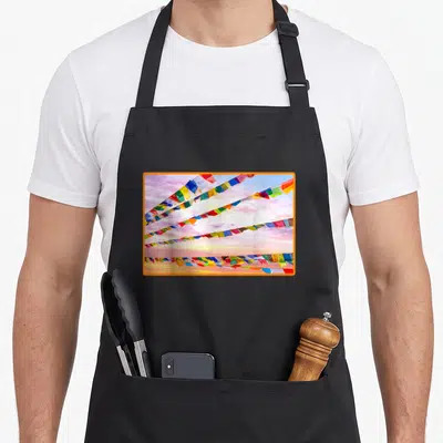 Tablier de cuisine noir avec des drapeaux de prière bouddhistes multicolores sur fond de ciel nuageux rosé.