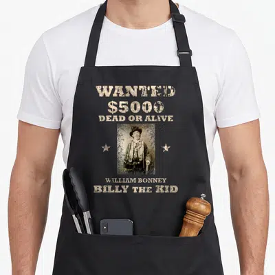 Tablier de cuisine noir avec une illustration vintage d'un homme en chapeau et les mots WANTED BILLY THE KID imprimés en beige.