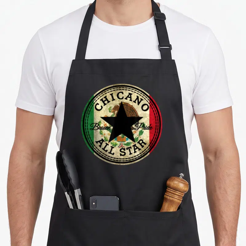 Tablier de cuisine noir avec un motif circulaire Chicano Brown Pride All Star sur fond texturé beige.