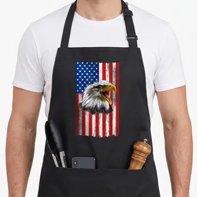 Tablier de cuisine noir avec tête d'aigle à tête blanche et drapeau américain en arrière-plan texturé.