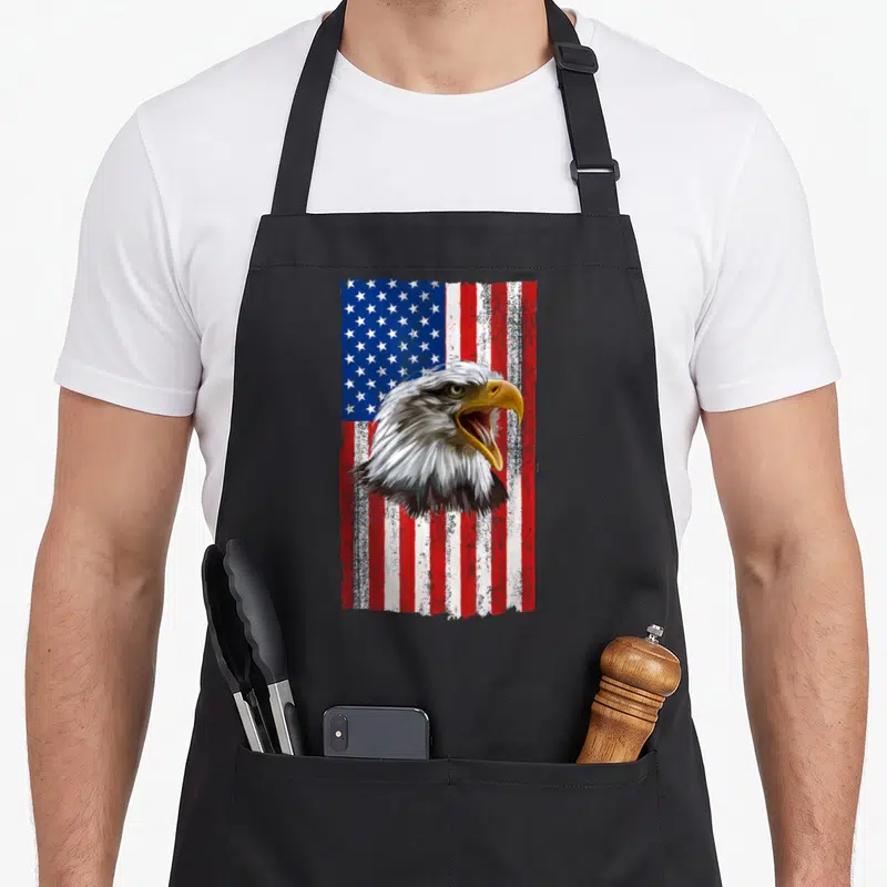 Tablier de cuisine noir avec tête d'aigle à tête blanche et drapeau américain en arrière-plan texturé.