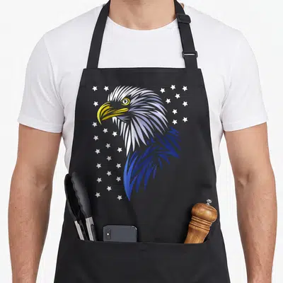 Tablier de cuisine noir avec tête d'aigle stylisée en bleu et blanc, entourée d'étoiles blanches sur fond gris.