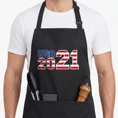 Tablier de cuisine noir avec l'inscription USA 2021 stylisée aux étoiles et bandes rouges et blanches du drapeau américain.