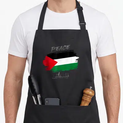 Tablier de cuisine noir avec une illustration brossée du drapeau palestinien et les mots Peace Palestine en anglais et en arabe.