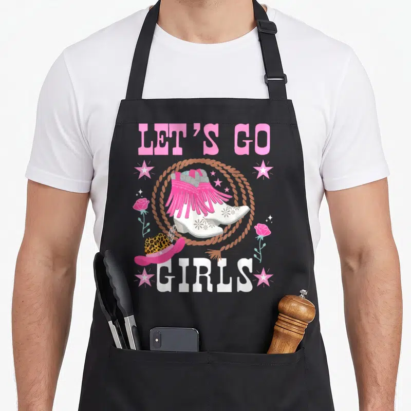 Tablier de cuisine noir avec bottes roses frangées, chapeau léopard et texte Let's Go Girls entourés d'un lasso et de roses.