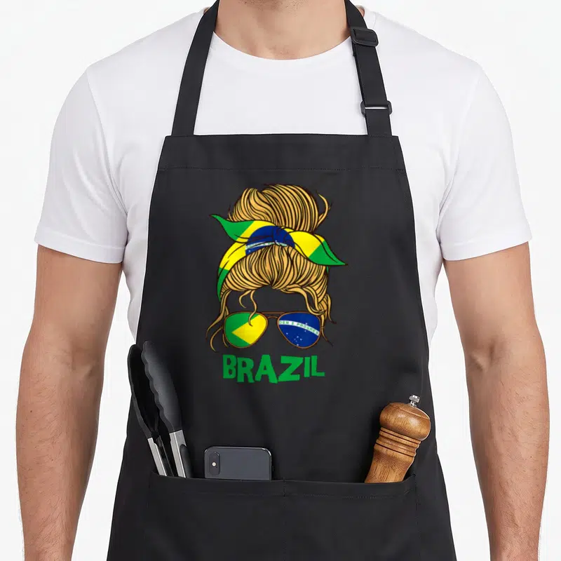 Tablier de cuisine noir avec illustration d'un chignon blonde, bandana tricolore et lunettes reflétant le drapeau brésilien.