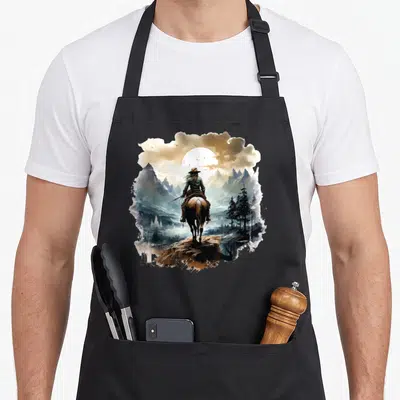 Tablier de cuisine noir avec illustration d'une cowgirl à cheval face à un paysage montagneux et une lune éclatante.