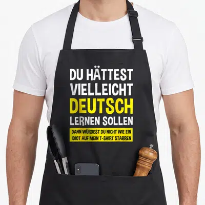 Tablier de cuisine noir avec inscription humoristique en allemand sur fond blanc et jaune vif.