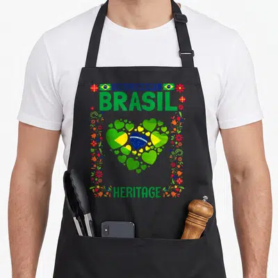 Tablier de cuisine noir avec un grand cœur composé de drapeaux brésiliens et le texte Orgullosamente Brasil Heritage entouré de fleurs.