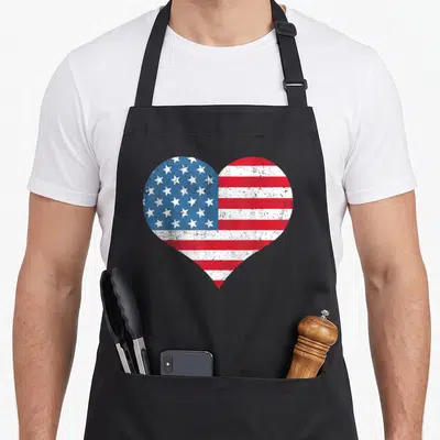Tablier de cuisine noir avec un grand motif cœur intégrant les étoiles et bandes du drapeau américain dans un style vieilli.