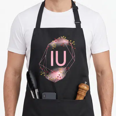 Tablier de cuisine noir avec le sigle IU en rose, encadré par un polygone géométrique et des coeurs rouges et dorés dispersés.