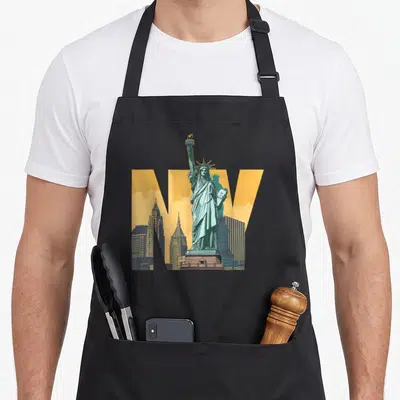 Tablier de cuisine noir avec Statue de la Liberté, lettres NY jaunes et silhouettes d'immeubles new-yorkais.