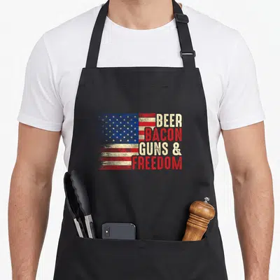 Tablier de cuisine noir avec drapeau américain vintage et texte BEER BACON GUNS & FREEDOM imprimé en rouge et blanc cassé.