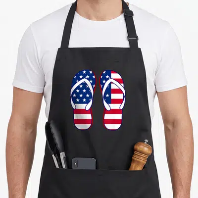 Tablier de cuisine noir avec illustration de deux sandales patriotiques au drapeau américain, étoiles et bandes rouges blanches bleues.