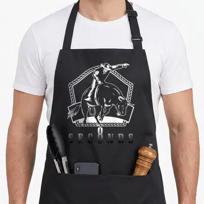 Tablier de cuisine noir avec illustration blanche d'un cowboy sur taureau et texte Ask Me In Eight Seconds au dos.