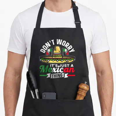 Tablier de cuisine noir avec un sombrero coloré, des drapeaux et le texte Ne Vous Inquiétez Pas C'est Juste Un Truc Mexicain.