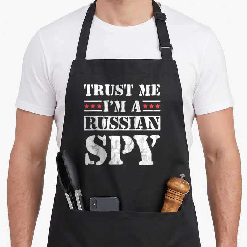 Tablier de cuisine noir avec inscription blanche « TRUST ME I'M A RUSSIAN SPY » et étoiles rouges stylisées.