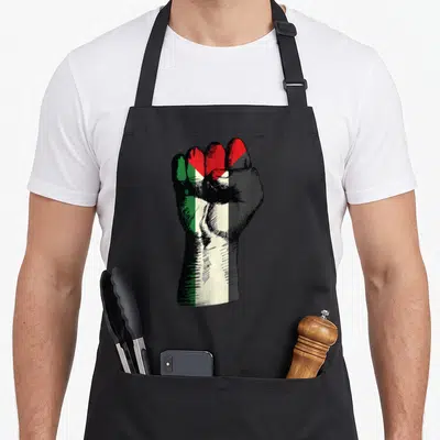 Tablier de cuisine noir avec un poing fermé aux couleurs du drapeau palestinien et le texte #FreePalestine en haut.