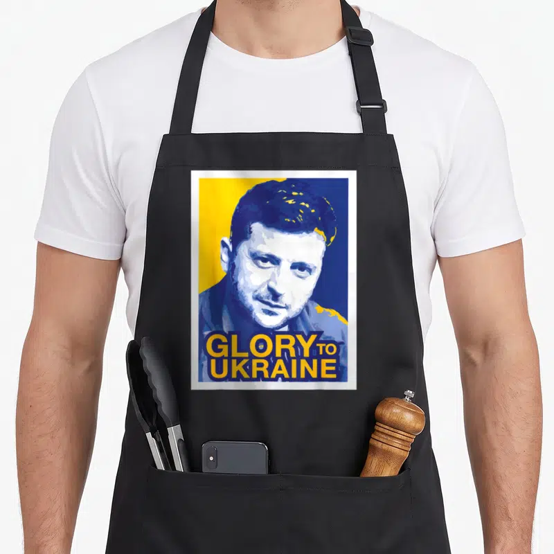 Tablier de cuisine noir avec portrait stylisé et inscription Glory to Ukraine en jaune et bleu.
