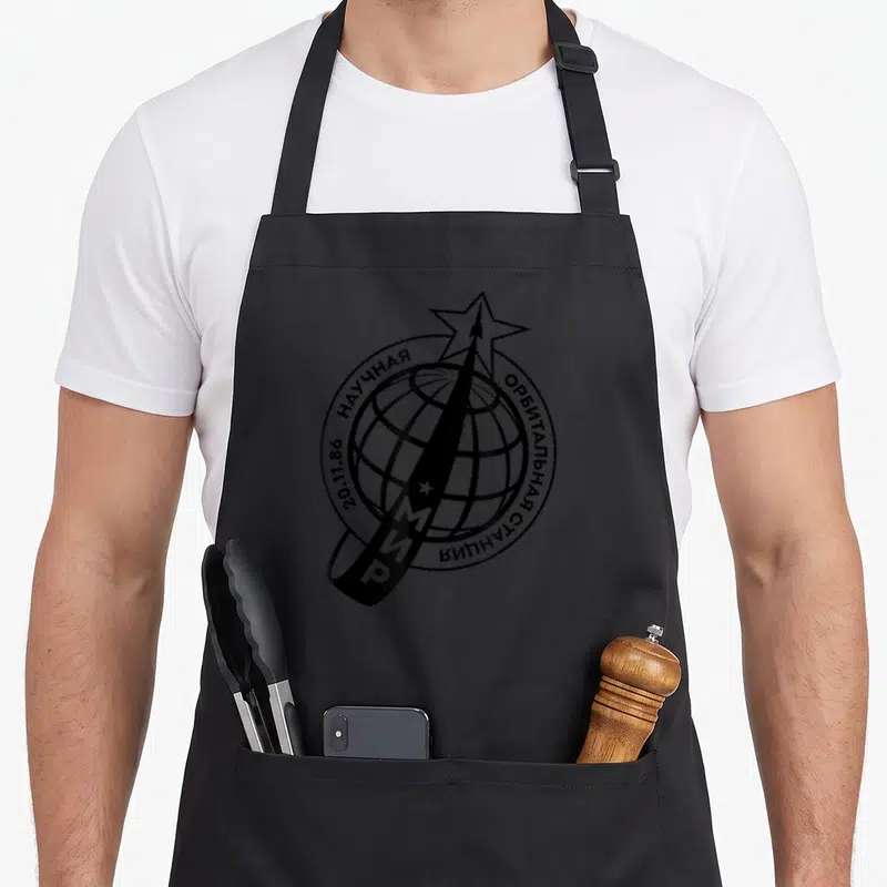 Tablier de cuisine noir avec l'emblème d'une station spatiale soviétique et une fusée traversant un globe.